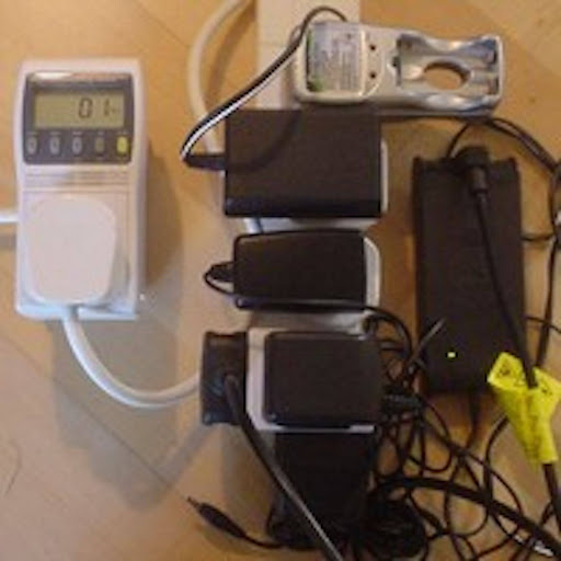 A power strip with five or more chargers plugged into it, with a meter reading the power usage at one watt.